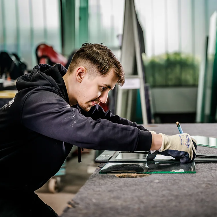 Junger Glaser Jülich von Glas Plum arbeitet konzentriert an einer Glasscheibe.